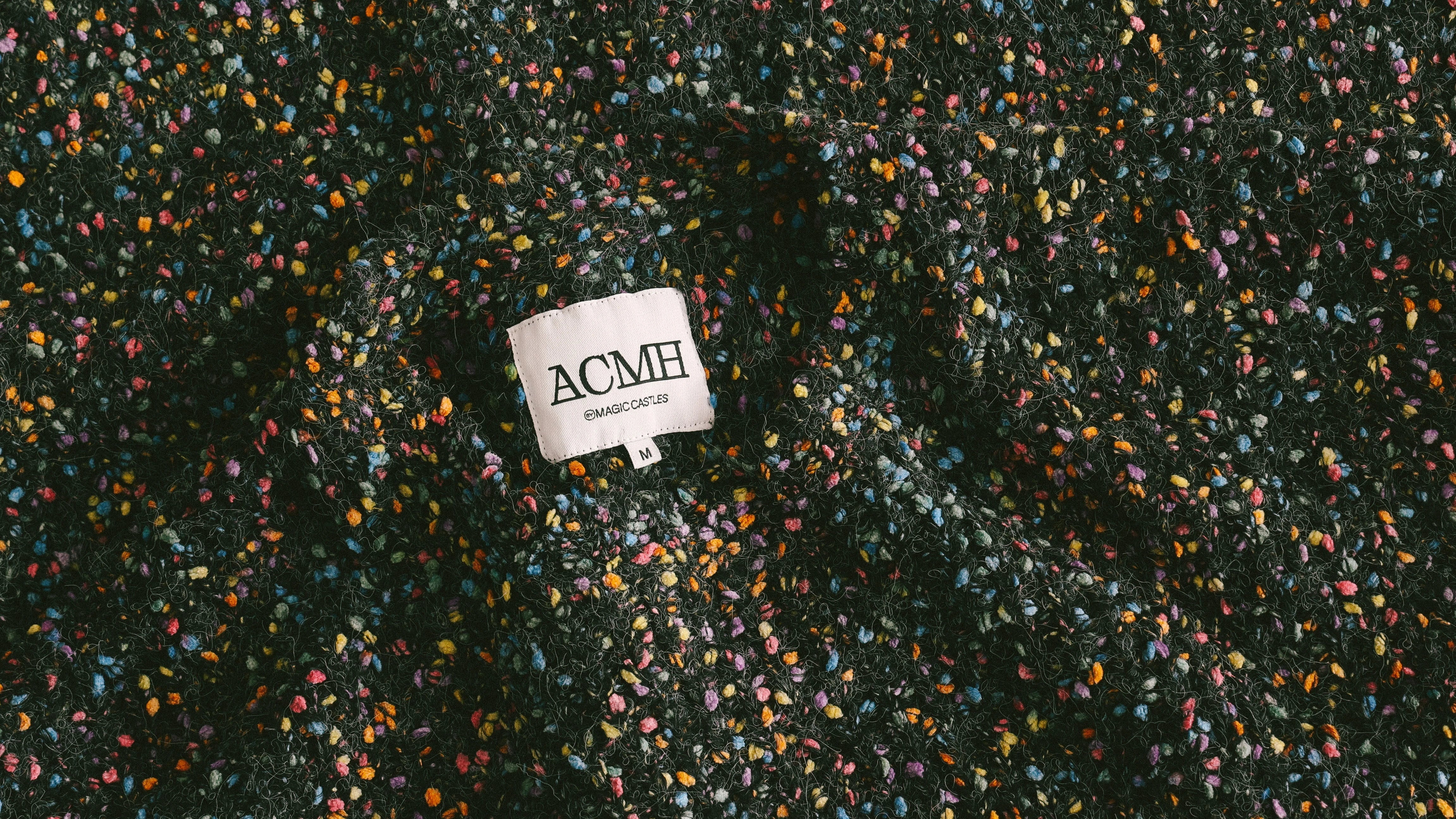 Flat lay of five folded shirts on a wooden floor, including graphic tees and collared shirts in various colors and patterns, featuring text designs like “Changing Constants” and “ACMH”.