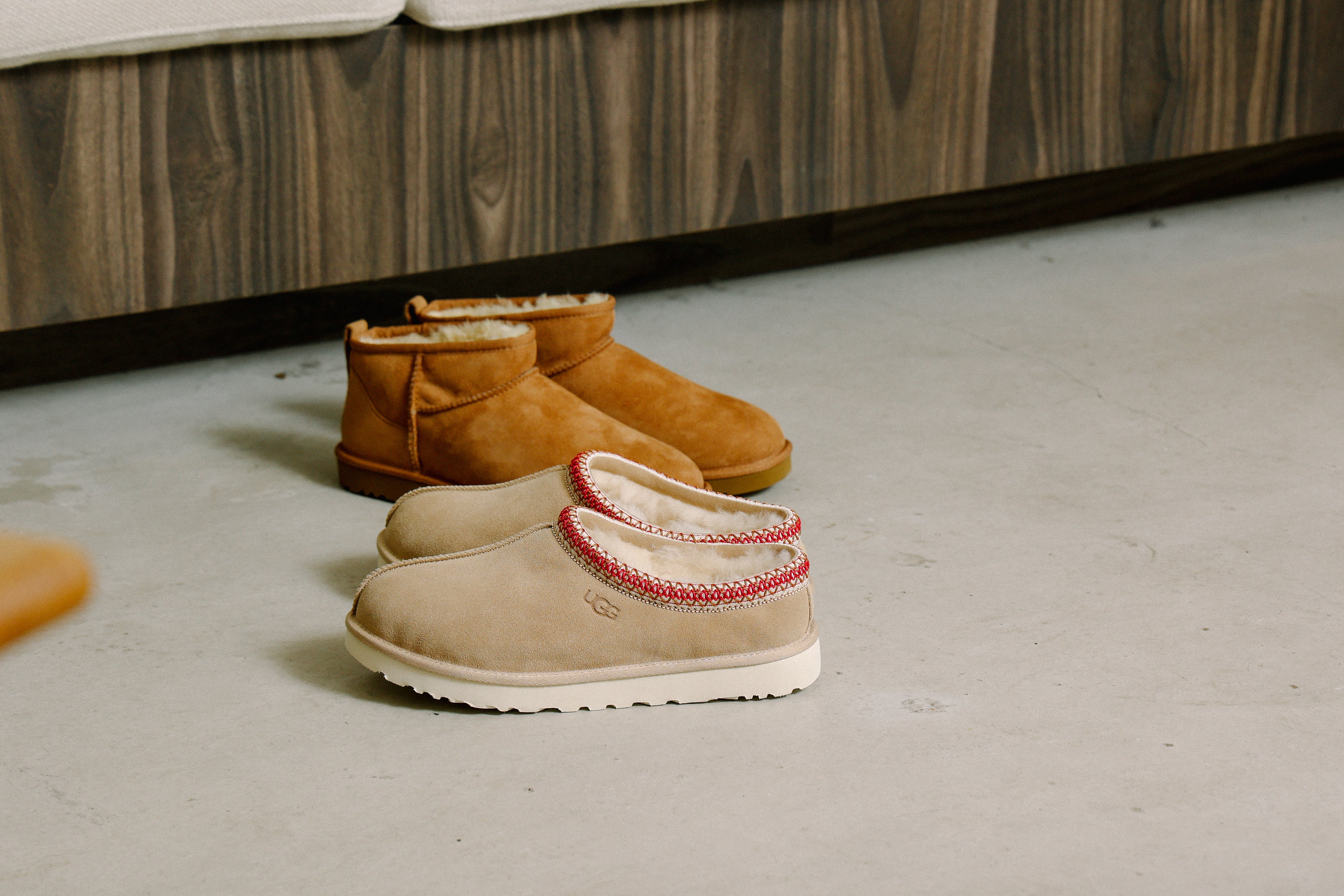 UGG Tasman slippers with a low slip-on design, suede upper, soft shearling lining, thick rubber sole, and decorative woven trim around the collar.