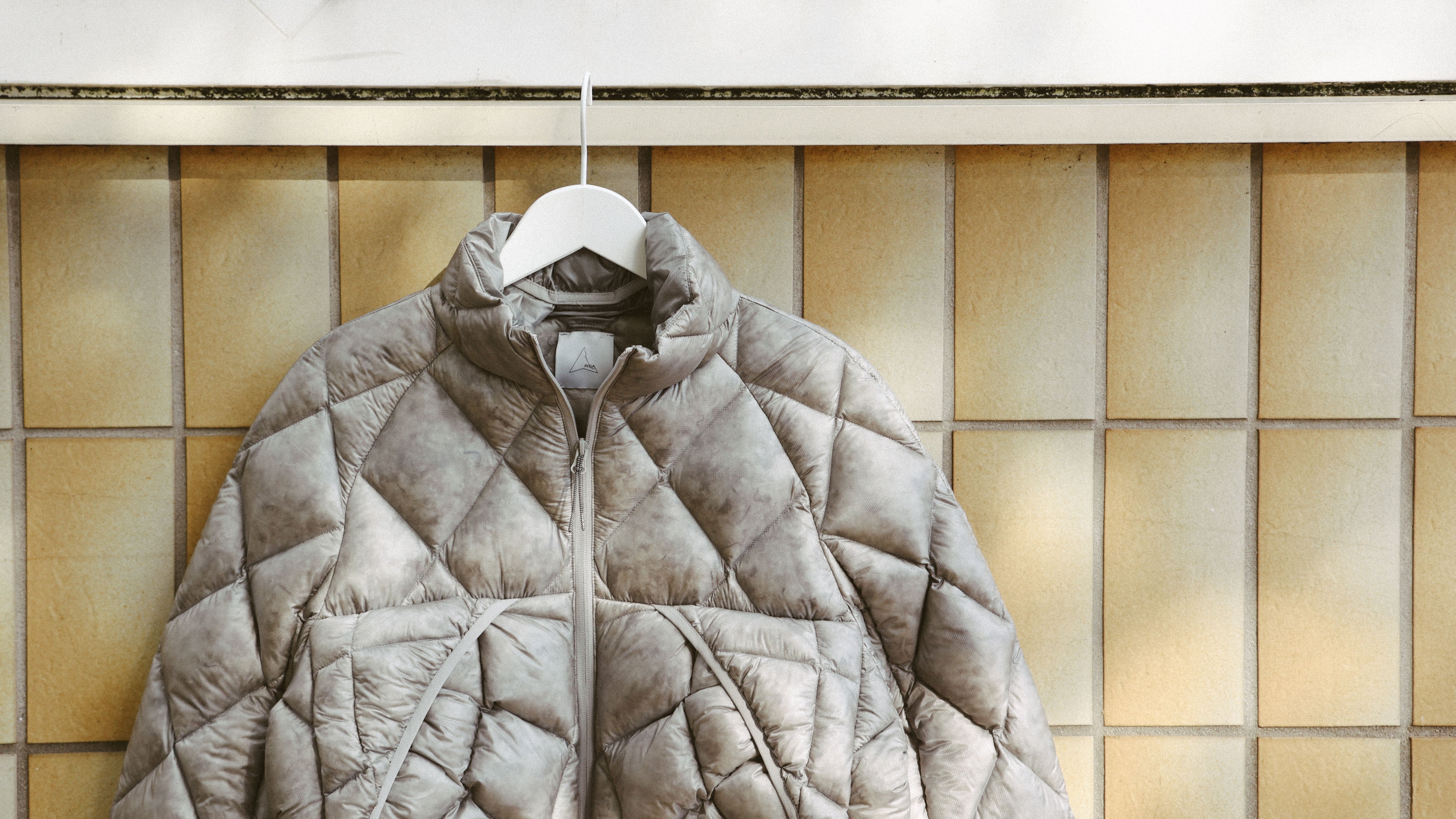 A brown and black ankle-high ROA hiking boot held in a hand with the ROA logo visible. The background is green bushes.